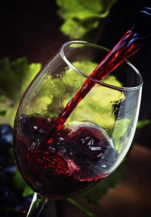 Red wine pouring into a glass, vintage wood background, selective focus