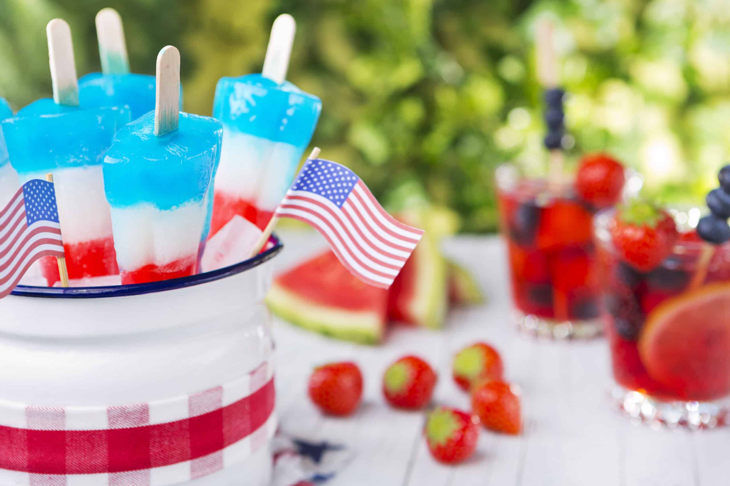 Red-white-and-blue popsicles on an outdoor table with summer drinks