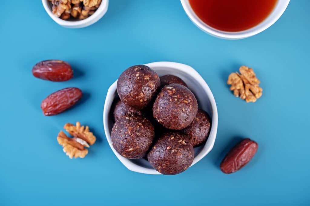 Nuts dates cocoa powder vegetarian balls in a white bowl on a blue background
